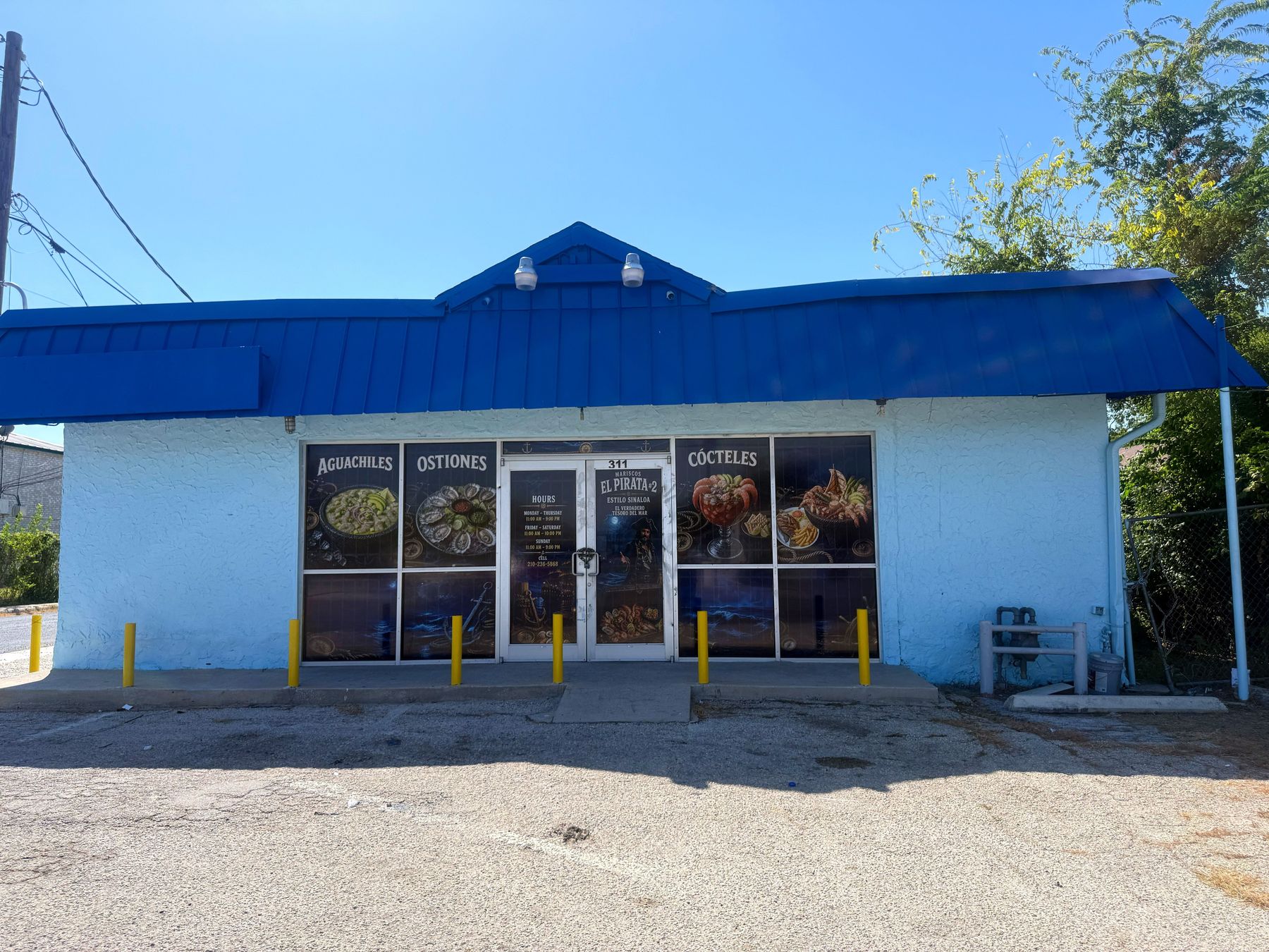 El frente de Mariscos El Pirata #2: techo azul cobalto, muros blancos y el número 311 sobre la puerta