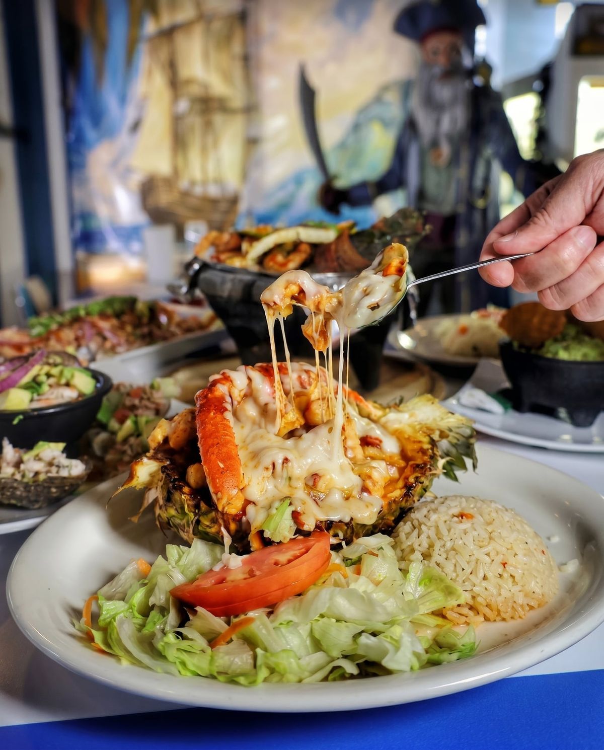 Piña a la Salsa Diablo — Una piña entera, ahuecada y rellena de mariscos en salsa diabla, con queso gratinado encima. Llega a la mesa y todos voltean. Es el platillo que la gente pide sin haberlo visto en el menú.